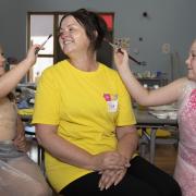 Two girls painting staff member's face at St James' summer club in Renfrew